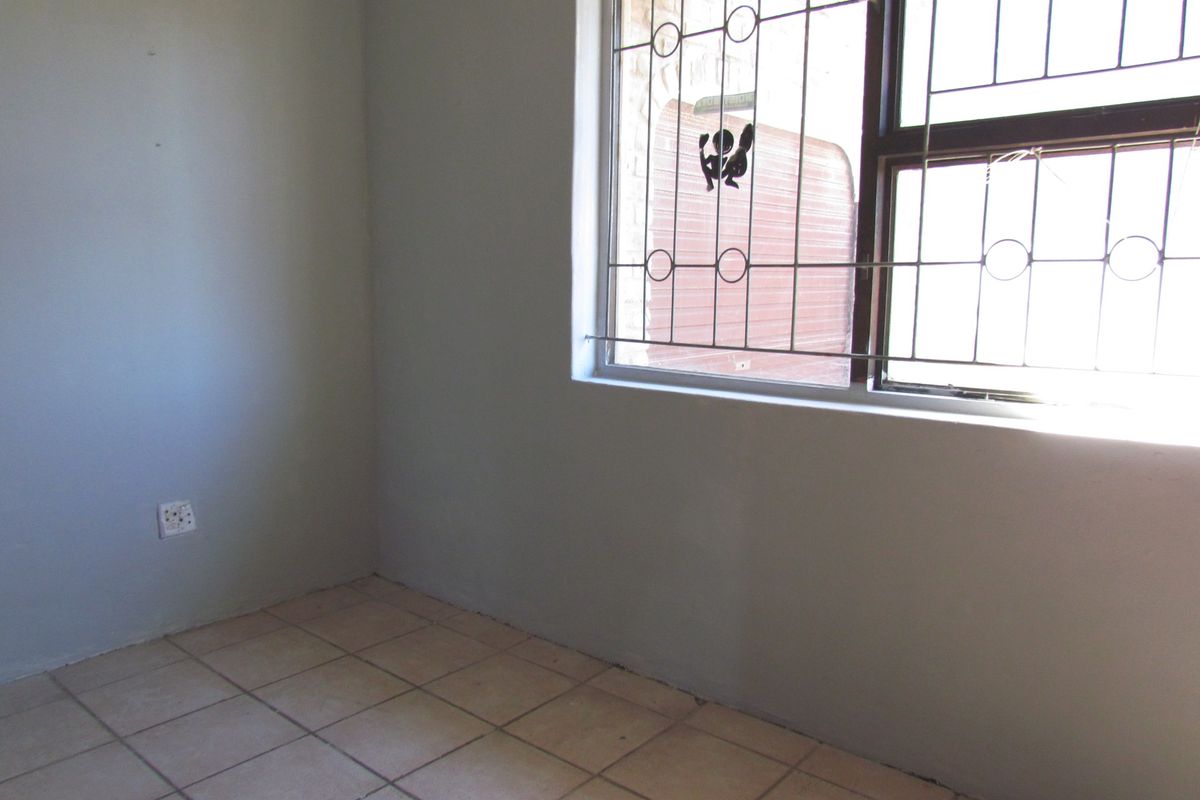 An empty bedroom featuring tiled flooring and security burglar bars on the window, providing a blank canvas for potential interior design updates.