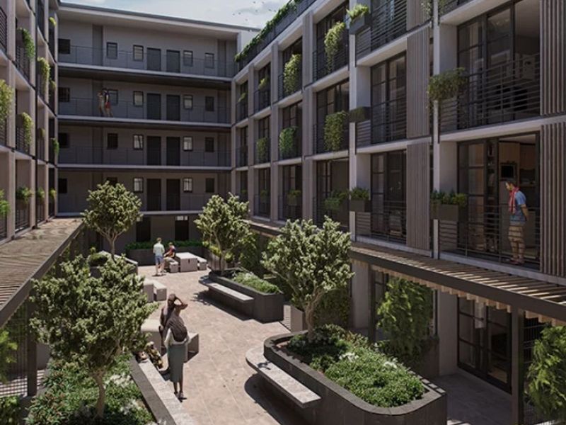 A modern apartment complex courtyard featuring landscaped gardens, raised concrete planters, a pergola, and private balconies overlooking the communal outdoor space.