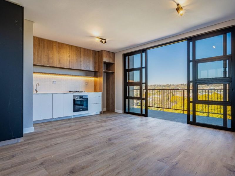Modern open-plan kitchen and living area featuring sleek cabinetry, integrated appliances, and large sliding doors opening to a balcony with scenic views.