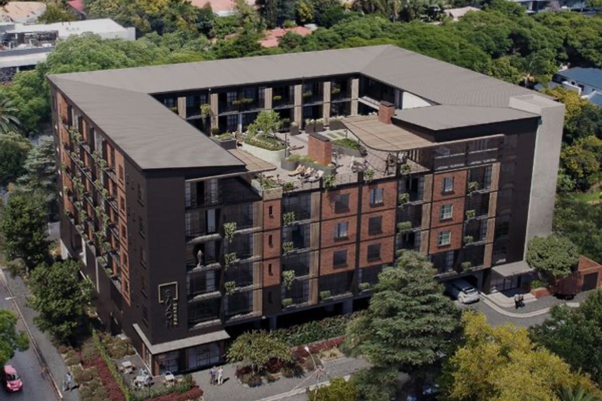 Aerial view of a modern multi-story apartment complex featuring a rooftop terrace, brick facade, and surrounding landscaped grounds in a suburban setting.