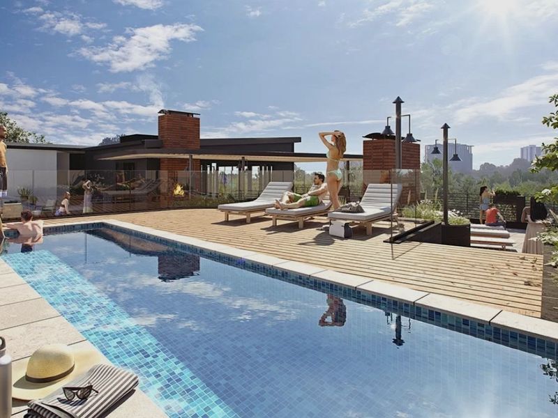 A modern rooftop pool area featuring timber decking, a glass balustrade, and a brick fireplace, offering a sophisticated outdoor leisure space.