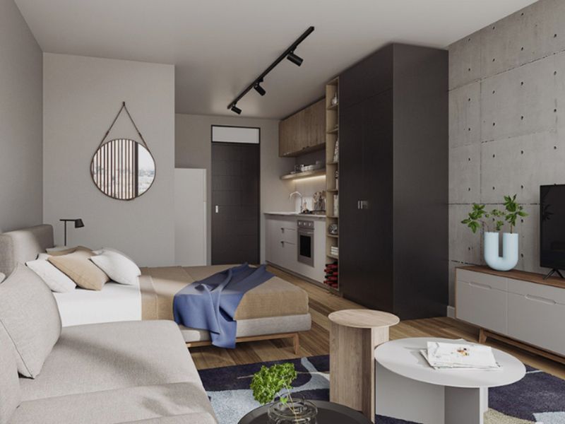 Modern open-plan studio apartment featuring a sleek kitchenette, exposed concrete accent wall, track lighting, and high-quality hardwood flooring throughout.
