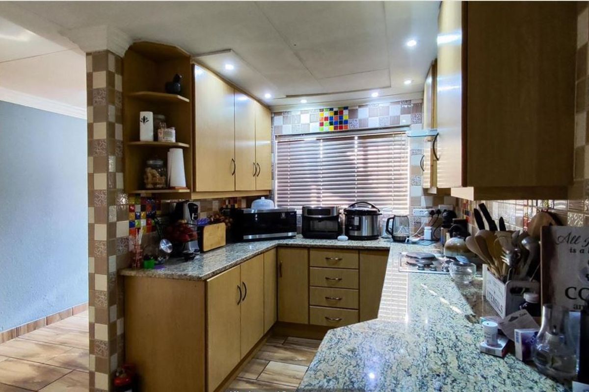 A functional kitchen featuring granite countertops, wooden cabinetry, and a tiled backsplash, offering a practical layout with integrated lighting.