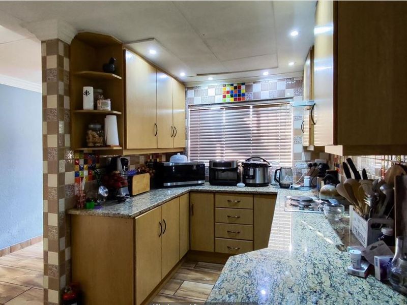 A functional kitchen featuring granite countertops, wooden cabinetry, and a tiled backsplash, offering a practical layout with integrated lighting.