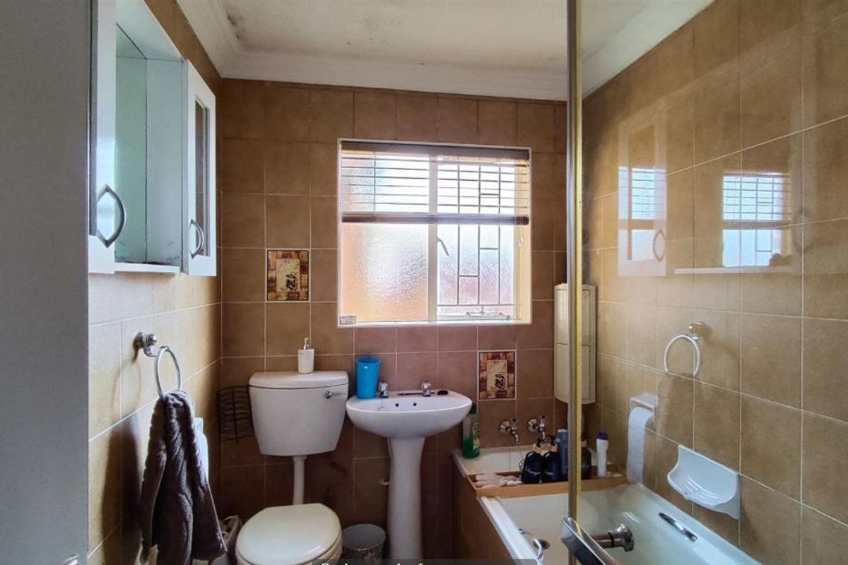 A compact bathroom featuring a pedestal basin, toilet, and bathtub with a glass shower screen, finished with full-height wall tiling.
