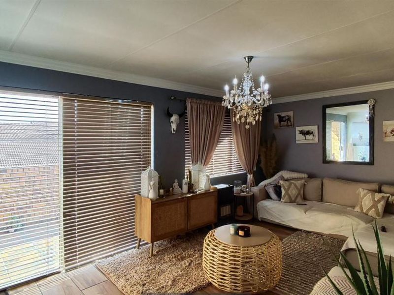 A well-maintained living room featuring tiled flooring, a large sliding glass door with venetian blinds, and elegant ceiling lighting.
