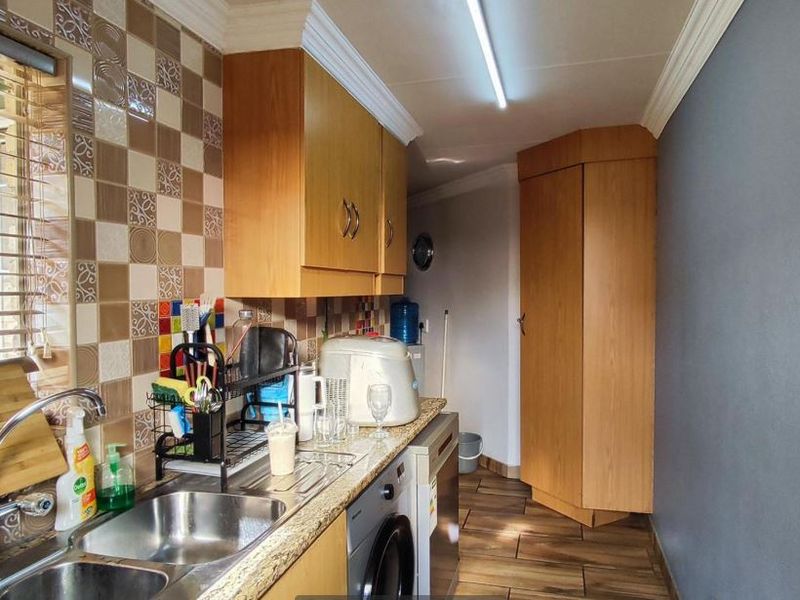 A functional kitchen featuring laminate cabinetry, a stainless steel sink, tiled backsplash, and wood-look floor tiles, offering practical storage and workspace.
