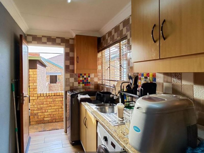 Compact scullery area featuring laminate cabinetry, granite countertops, stainless steel sink, and tiled backsplash with direct access to an outdoor area.