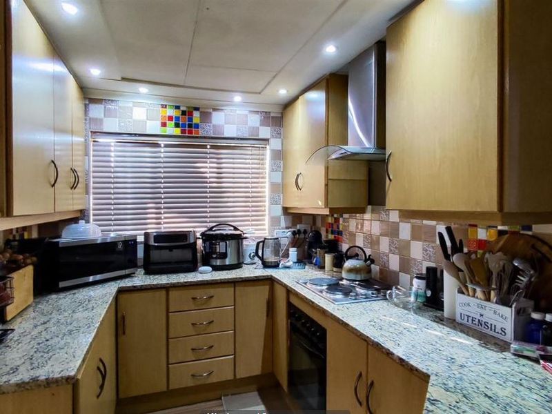 A functional U-shaped kitchen featuring laminate cabinetry, granite countertops, a built-in oven, electric hob, and a tiled backsplash with recessed lighting.