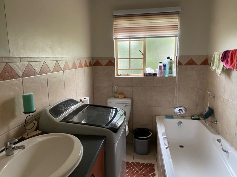 A functional bathroom featuring a built-in vanity, bathtub, and toilet, with tiled walls and a window providing natural light.