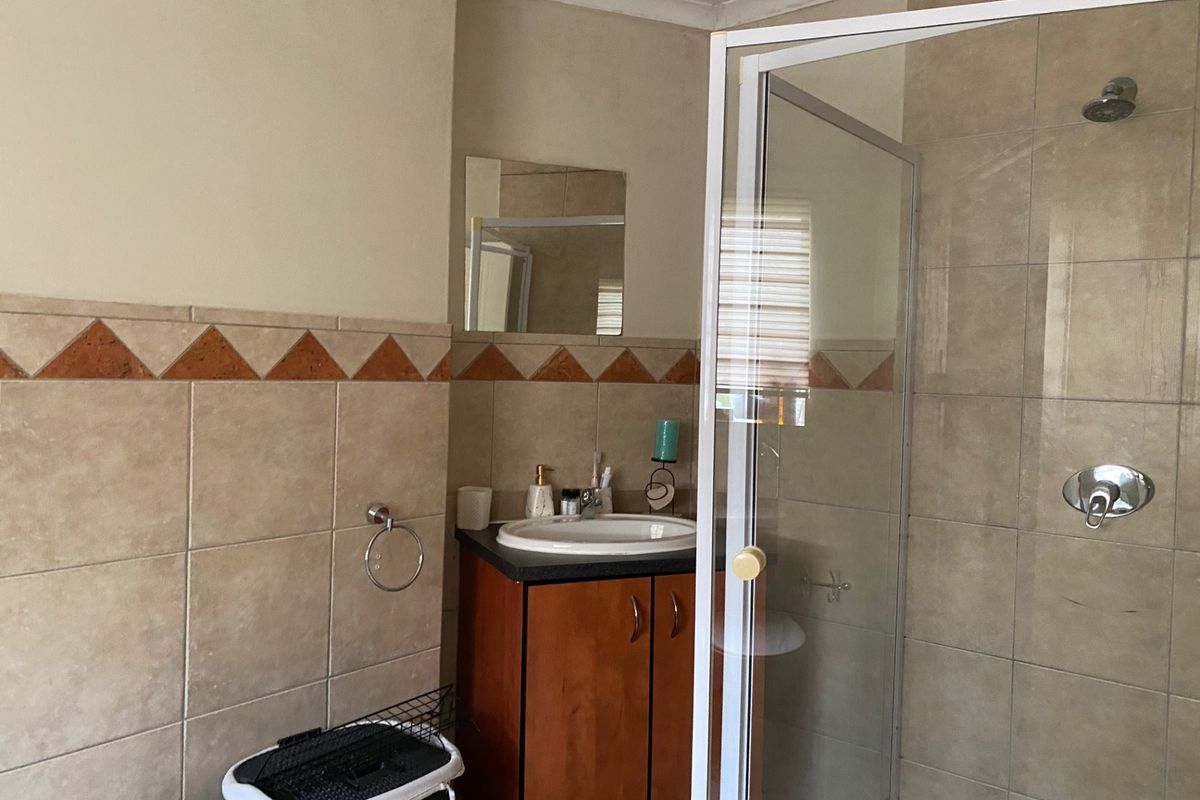 A functional bathroom featuring a shower enclosure, vanity cabinet with basin, and tiled walls with decorative border accents.