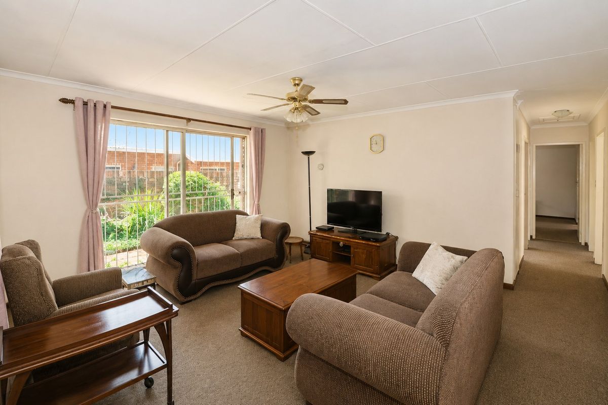 A comfortable living room featuring carpeted flooring, a ceiling fan, and a large sliding glass door with security bars leading to the exterior.