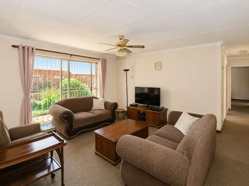 A comfortable living room featuring carpeted flooring, a ceiling fan, and a large sliding glass door with security bars leading to the exterior.