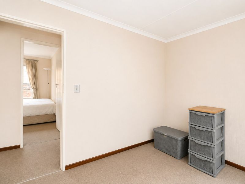 A neutral-toned bedroom featuring carpeted flooring, coved ceilings, and a doorway leading to an adjacent bedroom space.