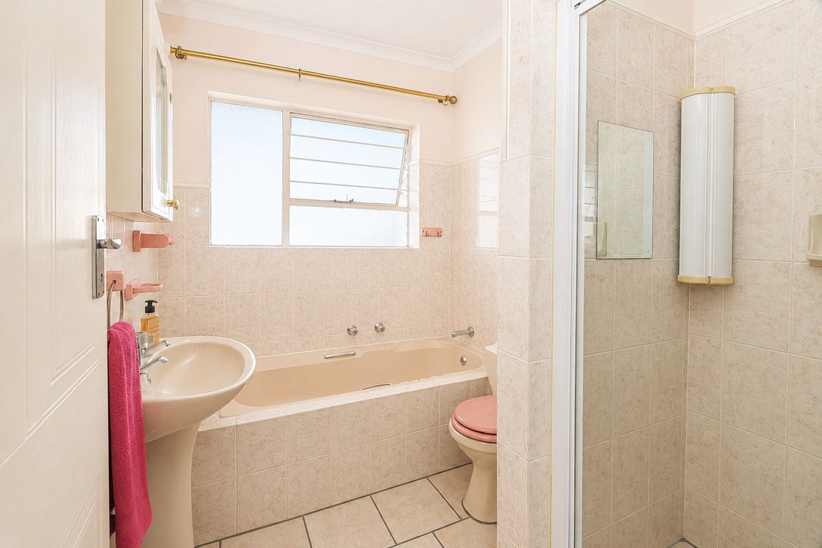A functional bathroom featuring a built-in bathtub, separate shower enclosure, pedestal basin, and toilet with neutral wall and floor tiling.