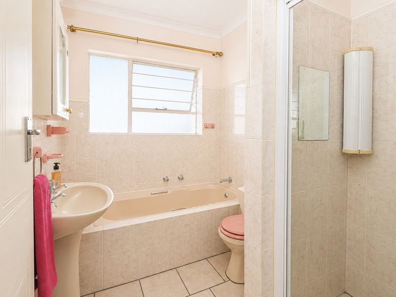 A functional bathroom featuring a built-in bathtub, separate shower enclosure, pedestal basin, and toilet with neutral wall and floor tiling.