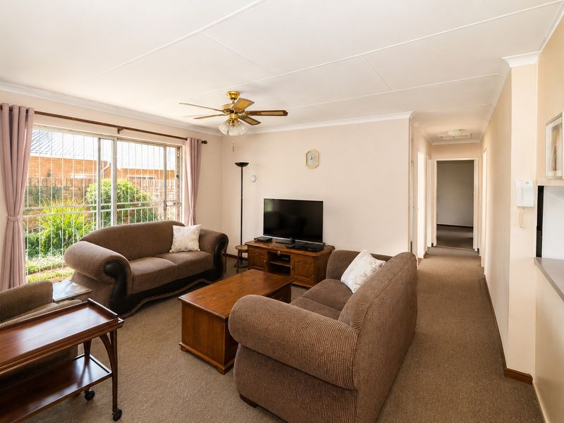 A comfortable living room featuring carpet flooring, a ceiling fan, and a sliding glass door with security bars providing natural light.