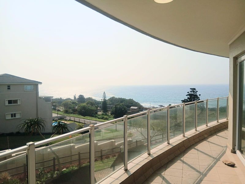 Spacious balcony featuring a modern glass balustrade and tiled flooring, offering expansive coastal and ocean views.