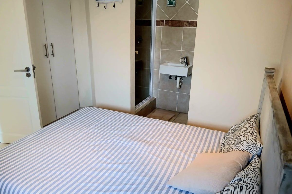Bedroom featuring a built-in wardrobe and a compact en-suite bathroom with a wall-mounted basin and shower enclosure.
