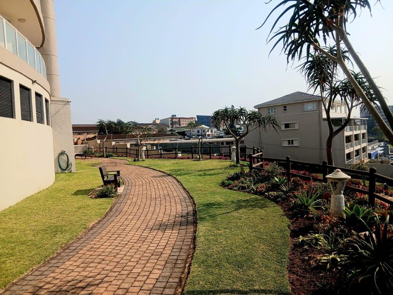 A well-maintained communal garden area featuring a paved walkway, manicured lawn, and established landscaping with timber fencing.