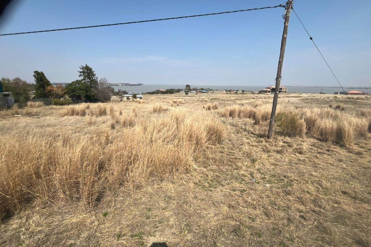 A wide-angle view of the vacant residential land featuring dry grass, a utility pole, and distant water views.