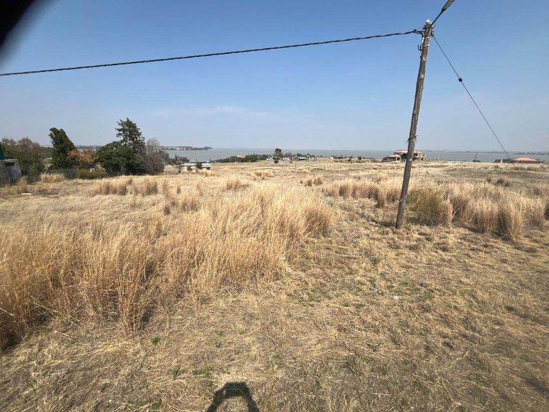 A wide-angle view of the vacant residential land featuring dry grass, a utility pole, and distant water views.