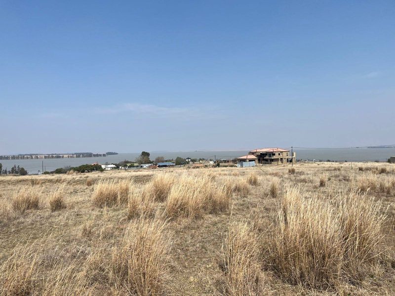 A wide-angle view of vacant residential land featuring dry grass and a scenic outlook over the nearby water.