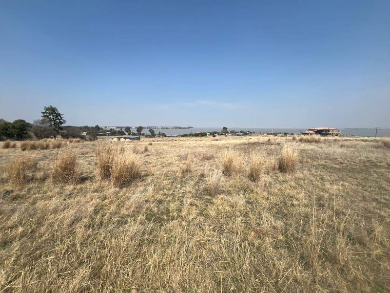 A wide-angle view of an expansive vacant residential plot featuring dry grass and a distant water outlook.