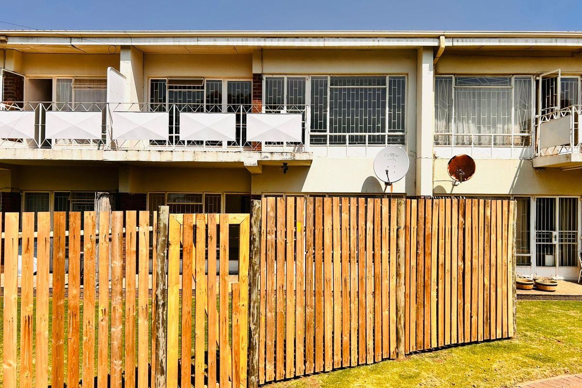 Rear elevation of a townhouse featuring a private garden with a wooden fence, upper-level balconies with security bars, and sliding door access.