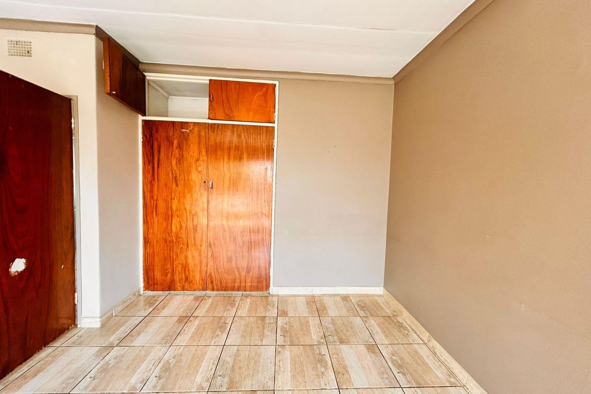 An empty bedroom featuring tiled flooring and built-in wooden cupboards with overhead storage compartments.