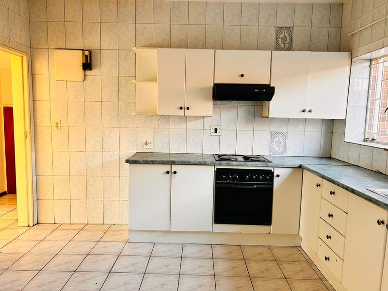 A dated kitchen featuring white cabinetry, laminate countertops, built-in oven, and hob, with full-height ceramic wall tiling and tiled flooring.