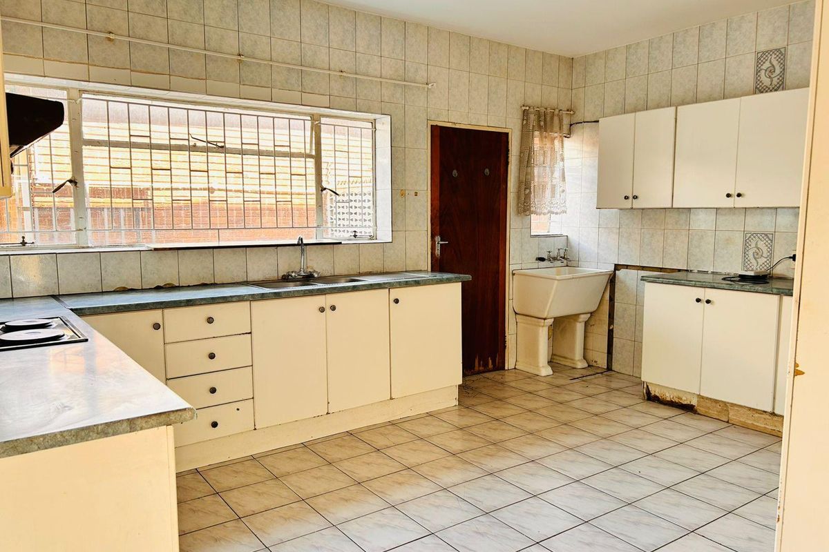 Spacious kitchen featuring original cabinetry, tiled surfaces, built-in hob, and a secondary pedestal sink, offering significant potential for a modern renovation.