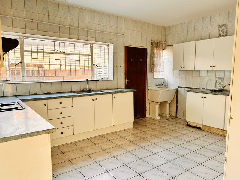 Spacious kitchen featuring original cabinetry, tiled surfaces, built-in hob, and a secondary pedestal sink, offering significant potential for a modern renovation.