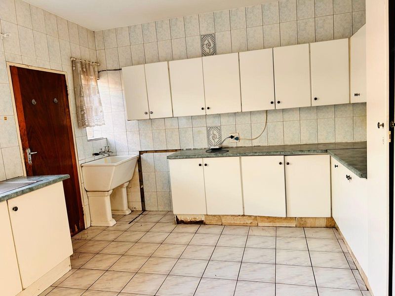 A dated kitchen featuring white cabinetry, laminate countertops, and ceramic tiling, currently in need of cosmetic updates and repairs to the cabinet base.