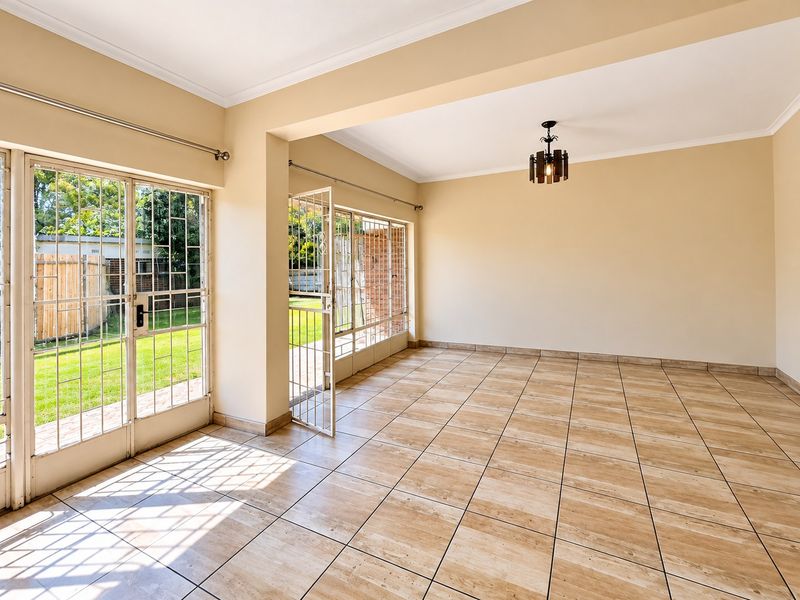 A bright, empty living room featuring neutral tiled flooring, cove cornicing, and large glass sliding doors providing direct access to the garden.