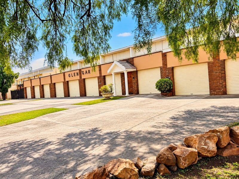 Front exterior view of the Glen Gar townhouse complex featuring multiple garage doors, a concrete driveway, and a covered entrance.