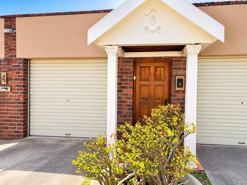 Front elevation of a townhouse featuring a double garage with roller doors, a covered entrance porch with decorative columns, and a solid timber front door.