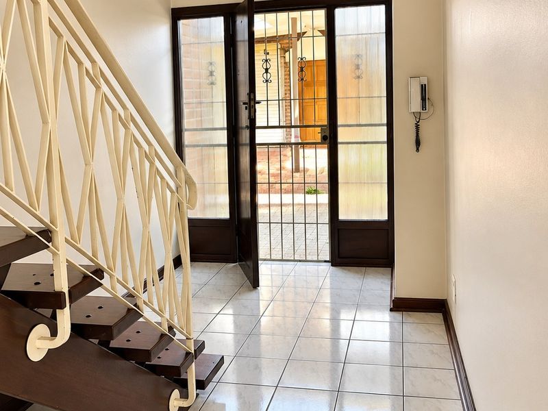 A bright entrance hall featuring tiled flooring, a staircase with a metal balustrade, and a secure entrance door with a security gate.