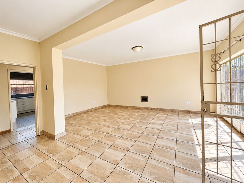 Spacious, empty living area featuring neutral ceramic floor tiles, a built-in wall heater, and direct access to an adjacent kitchen space.