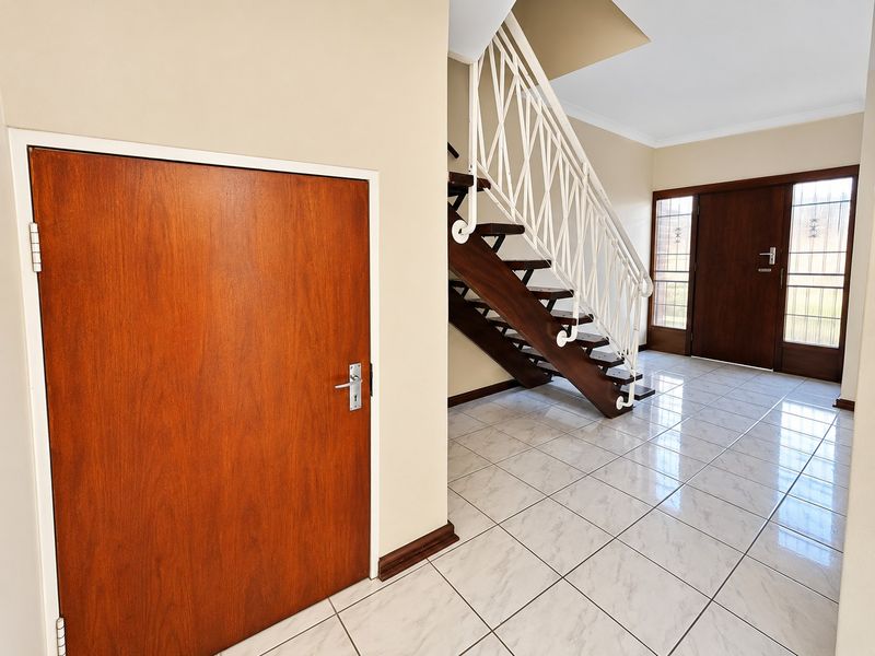 Spacious entrance hall featuring polished tiled flooring, a wooden staircase with a decorative metal balustrade, and a solid timber front door with sidelight windows.