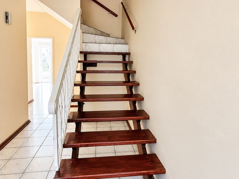 A bright hallway featuring an open-tread timber staircase with a metal balustrade and neutral tiled flooring leading to the upper level.