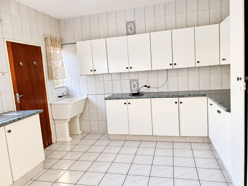 A functional kitchen featuring white cabinetry, laminate countertops, tiled flooring, and a pedestal utility sink, offering a clean and practical workspace.