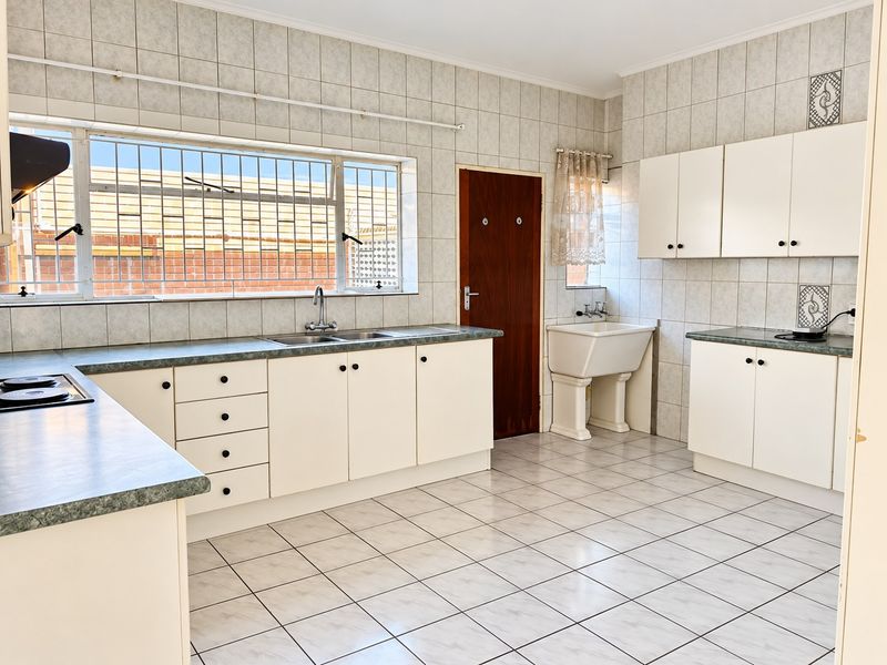 Spacious kitchen featuring built-in cabinetry, laminate countertops, double basin sink, and a separate butler sink, finished with ceramic wall and floor tiling.
