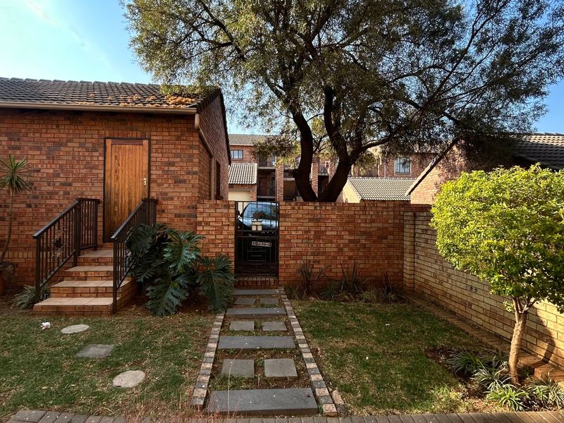 A rear exterior view of the apartment featuring a brick facade, a paved garden walkway, and a private gated entrance with external stairs.