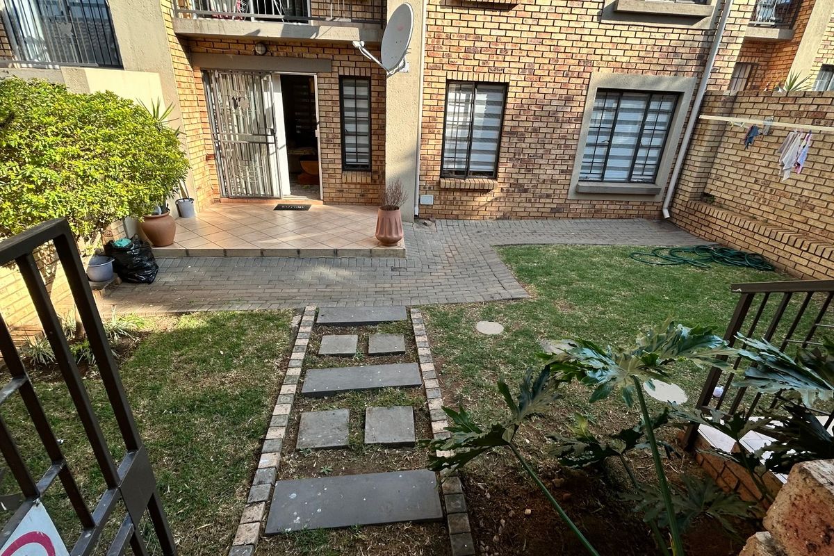 A private rear courtyard featuring a brick facade, paved patio area, and a small garden with a stone pathway leading to the entrance.