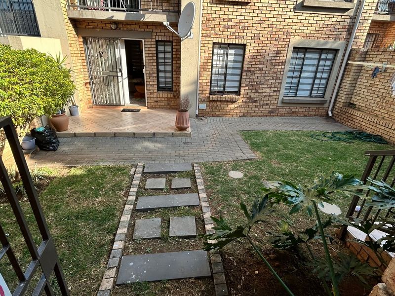 A private rear courtyard featuring a brick facade, paved patio area, and a small garden with a stone pathway leading to the entrance.