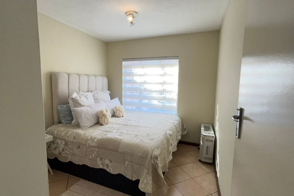 A functional bedroom featuring tiled flooring, a neutral color palette, and a window fitted with a modern roller blind.