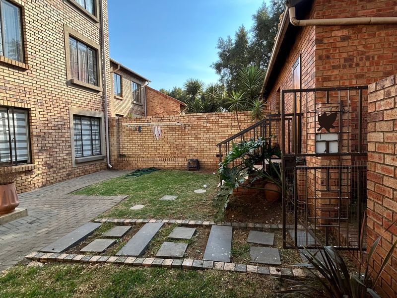 A private rear courtyard featuring a face brick exterior, paved patio area, small lawn, and secure metal gate access.