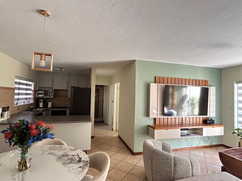 Open-plan living and kitchen area featuring tiled flooring, a modern built-in media console, and a functional kitchen with granite countertops and integrated appliances.