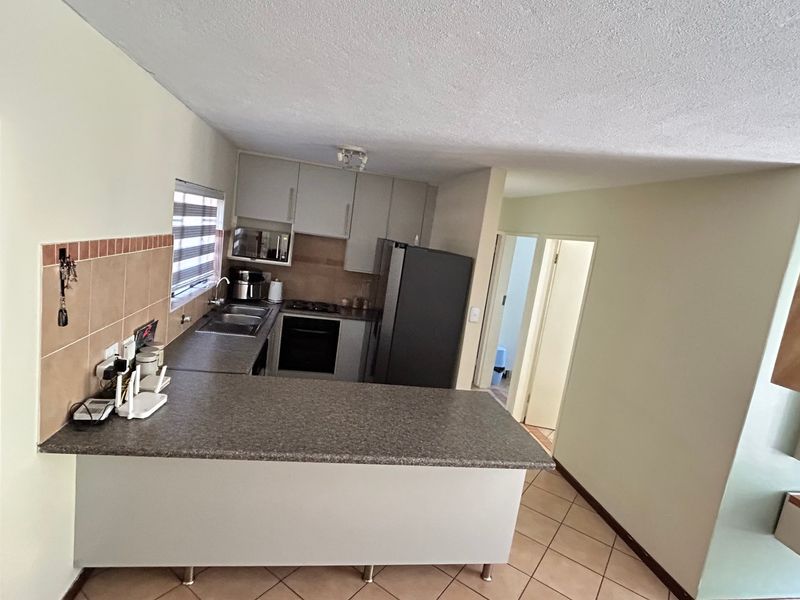 Open plan kitchen featuring laminate countertops, built-in cabinetry, and tiled flooring, seamlessly connecting to the living area and hallway.